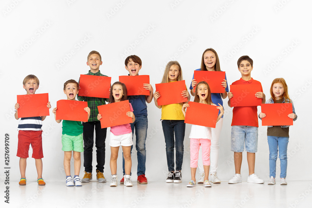Group of happy screaming children with a red empty banners isolated in white studio background. Education and advertising concept Group of happy screaming children with a red empty banners isolated in white studio background. Education and advertising concept