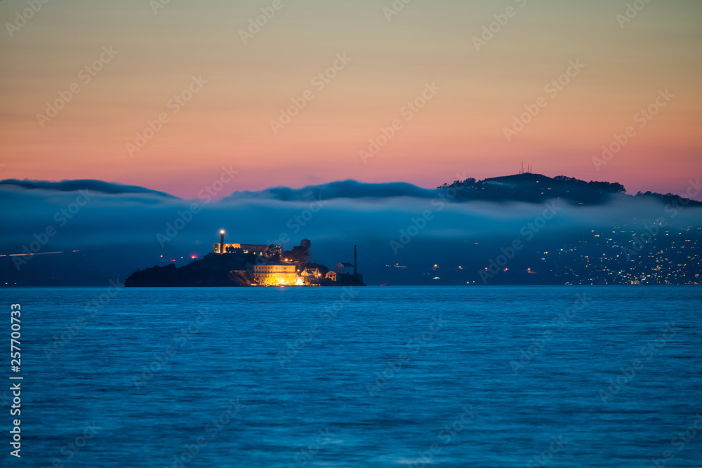 Fototapeta premium Alcatraz Island at sunset surrounded by fog and mountains
