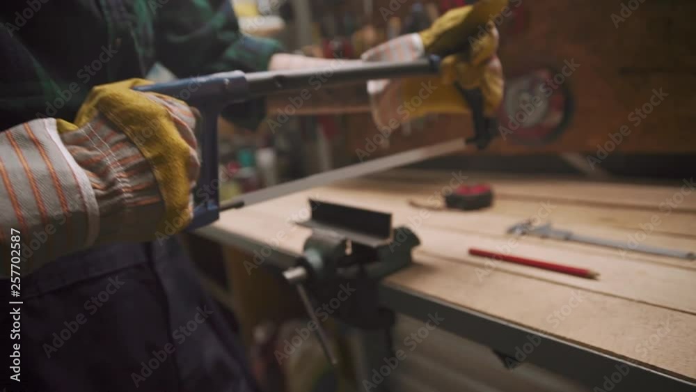 Close up view female hands cutting metal plate with hacksaw at workshop Close up view female hands cutting metal plate with hacksaw at workshop