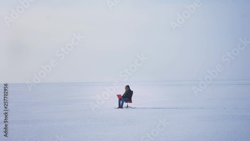 Wide shot of alone businessman in warm coat and hood sitting in snow desert and working with laptop attentively.