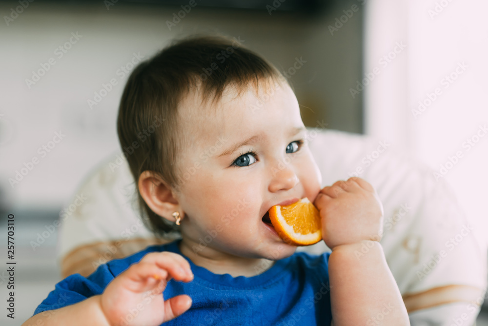 little girl sitting in baby chair, eating an orange little girl sitting in baby chair, eating an orange