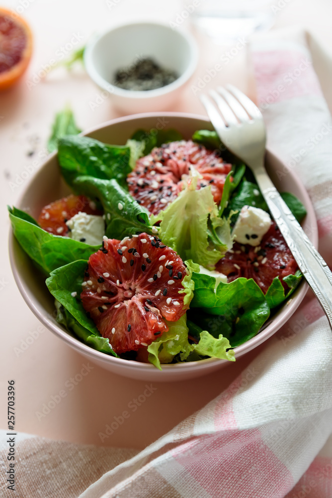 Spring fresh salad with blood orange, lettuce, spinach and sesame seeds on pink background. Top view. Selective focus Spring fresh salad with blood orange, lettuce, spinach and sesame seeds on pink background. Top view. Selective focus