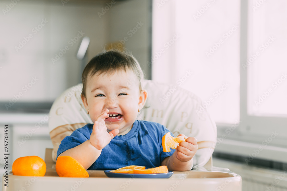 little girl sitting in baby chair, eating an orange little girl sitting in baby chair, eating an orange