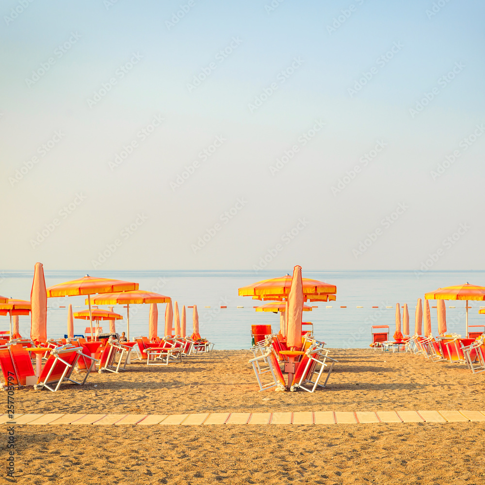 Tropical beach resort hotel background as summer landscape with lounge chairs and parasol in sun rays and calm sea. Tourism and travel, vacation, holiday destination concept Tropical beach resort hotel background as summer landscape with lounge chairs and parasol in sun rays and calm sea. Tourism and travel, vacation, holiday destination concept