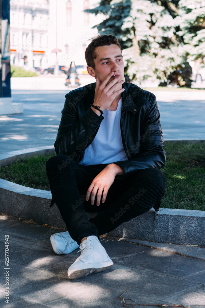 a young guy smokes around a tree in the city.bad habit.smoking in a public place a young guy smokes around a tree in the city.bad habit.smoking in a public place