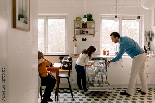Father and daughter arranging utensils in dishwasher photo