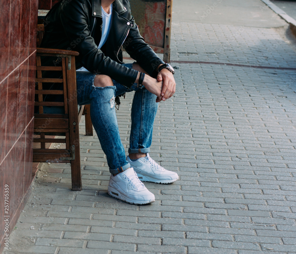 attractive guy sitting on a bench in a cafe, on the street, white sneakers,  white T-shirt, black leather jacket and black jeans, pants. model. waiting  for a meeting. Stock Photo | Adobe