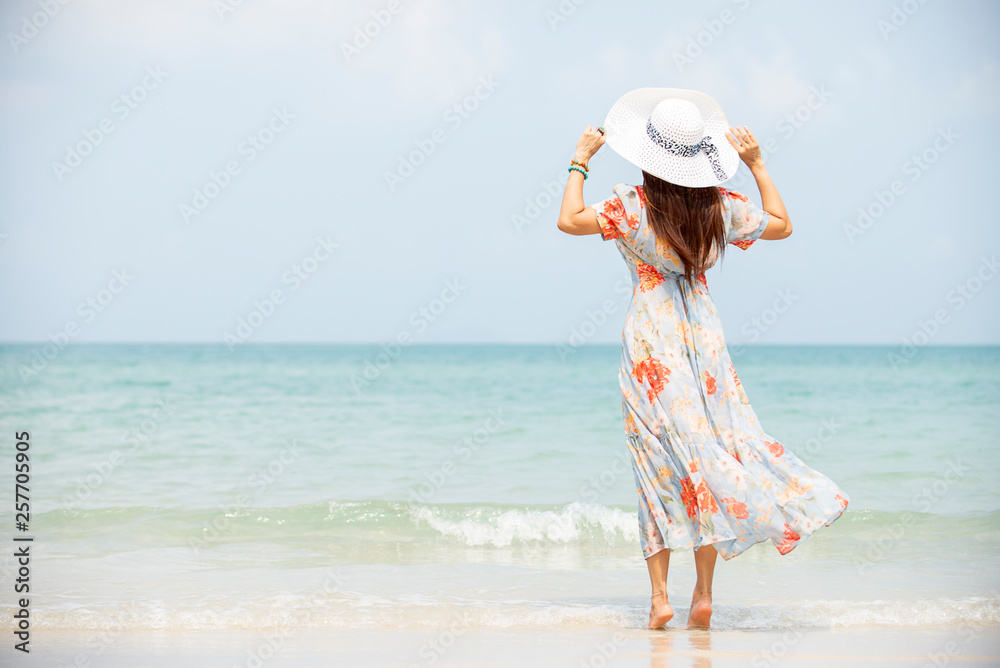 Happy traveler asia woman in dress holding sun hat standing on beach  enjoys her tropical  vacation