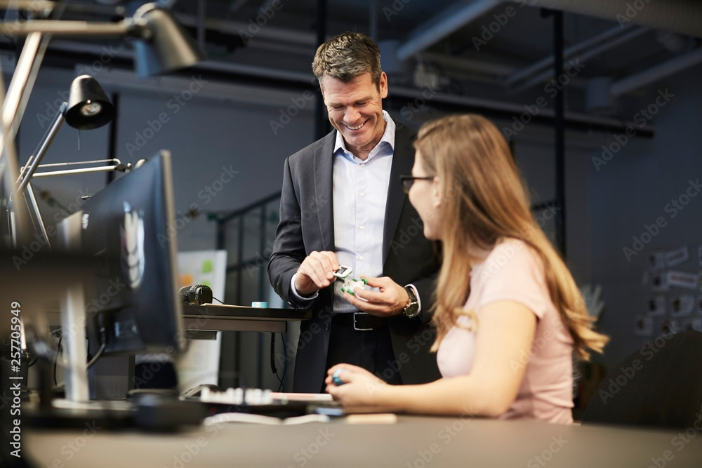 Creative businesswoman looking at smiling male bank manager holding solar toy car in creative office Creative businesswoman looking at smiling male bank manager holding solar toy car in creative office