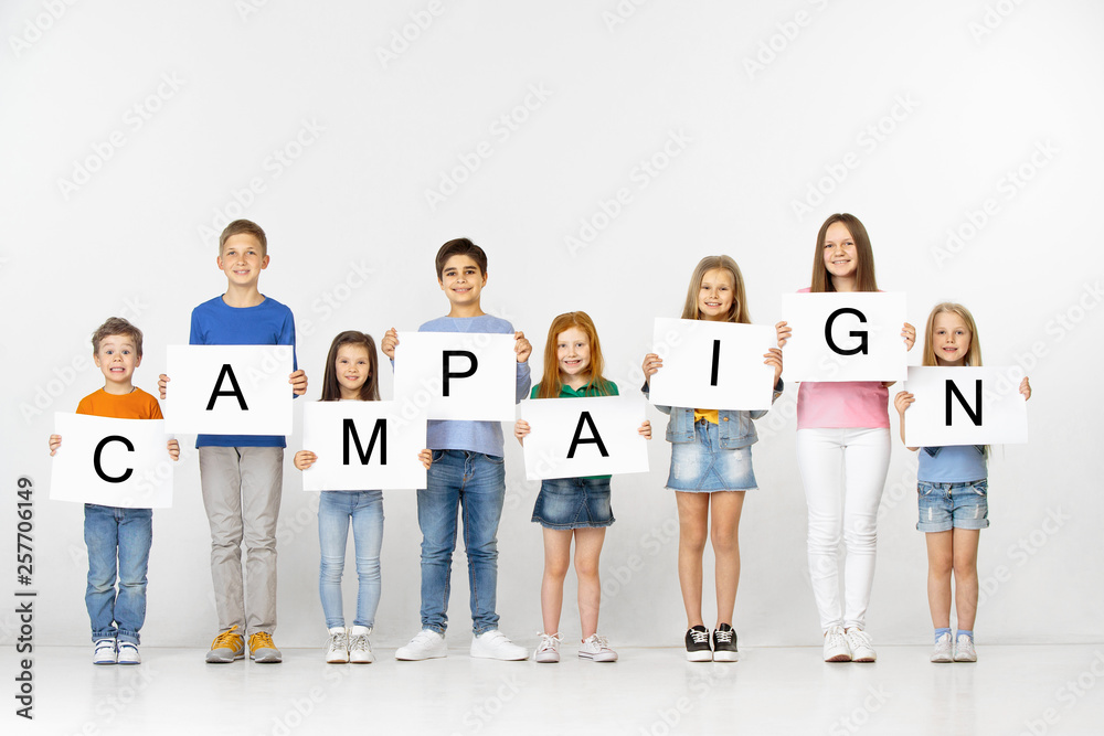 Campaign. Group of happy smiling children and teenagers or young team with a white banners holding word isolated in light studio background. Education and advertising concept. Campaign. Group of happy smiling children and teenagers or young team with a white banners holding word isolated in light studio background. Education and advertising concept.