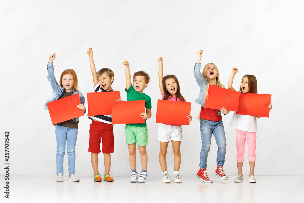 Fototapeta premium Group of happy smiling children with red empty banners isolated in white studio background. Education and advertising concept