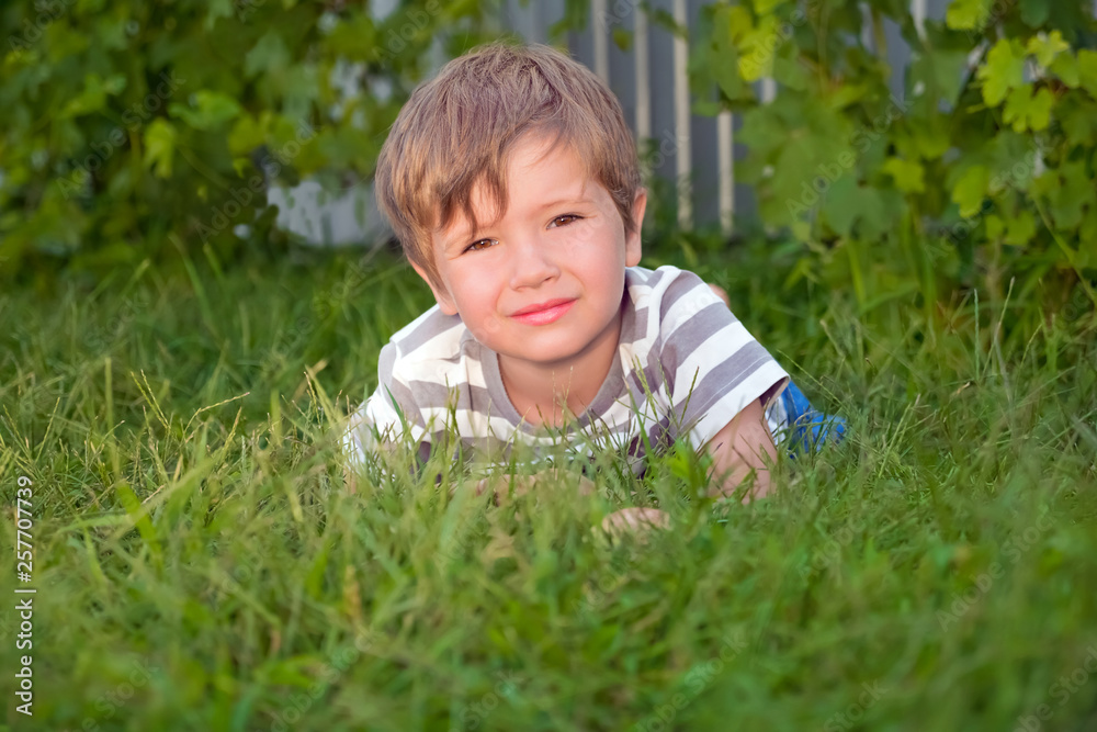 Smiling boy lying on green grass. Outdoor activities for children. Summer holidays concept. Training for children. Early start concept. Happy childhood concept. Positive emotions. Facial emotions Smiling boy lying on green grass. Outdoor activities for children. Summer holidays concept. Training for children. Early start concept. Happy childhood concept. Positive emotions. Facial emotions