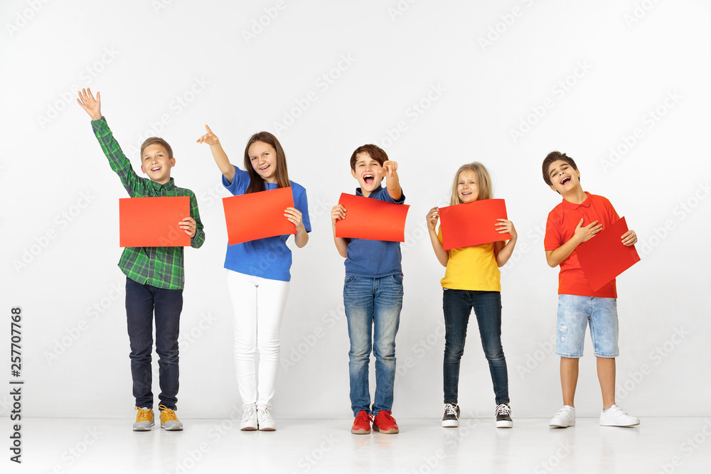 Group of happy smiling children with red empty banners isolated in white studio background. Education and advertising concept Group of happy smiling children with red empty banners isolated in white studio background. Education and advertising concept