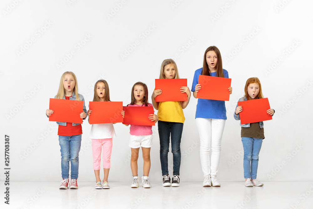 Fototapeta premium Group of happy surprised children with red empty banners isolated in white studio background. Education and advertising concept