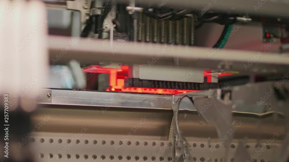 Electronic circuit in surface-mounting machine with red light, bottom view. Surface-mount technology as producing of electronic circuits. Components placed onto the surface of printed elements