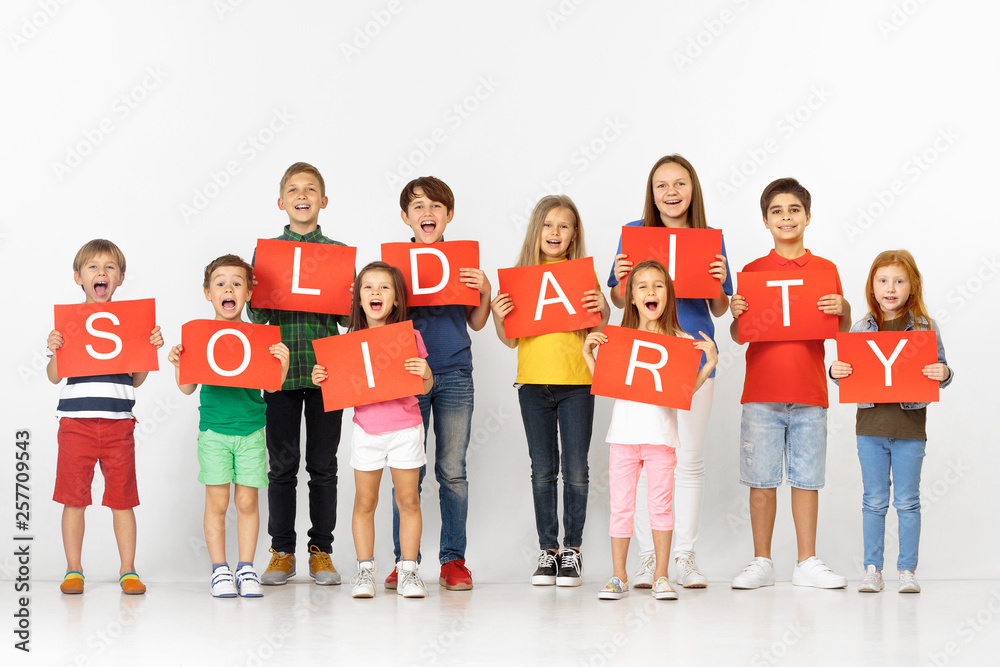 Obraz premium Solidarity of sweet hearts. Group of happy screaming children, young team or teenagers with a red banners isolated in white studio background. Education and advertising concept
