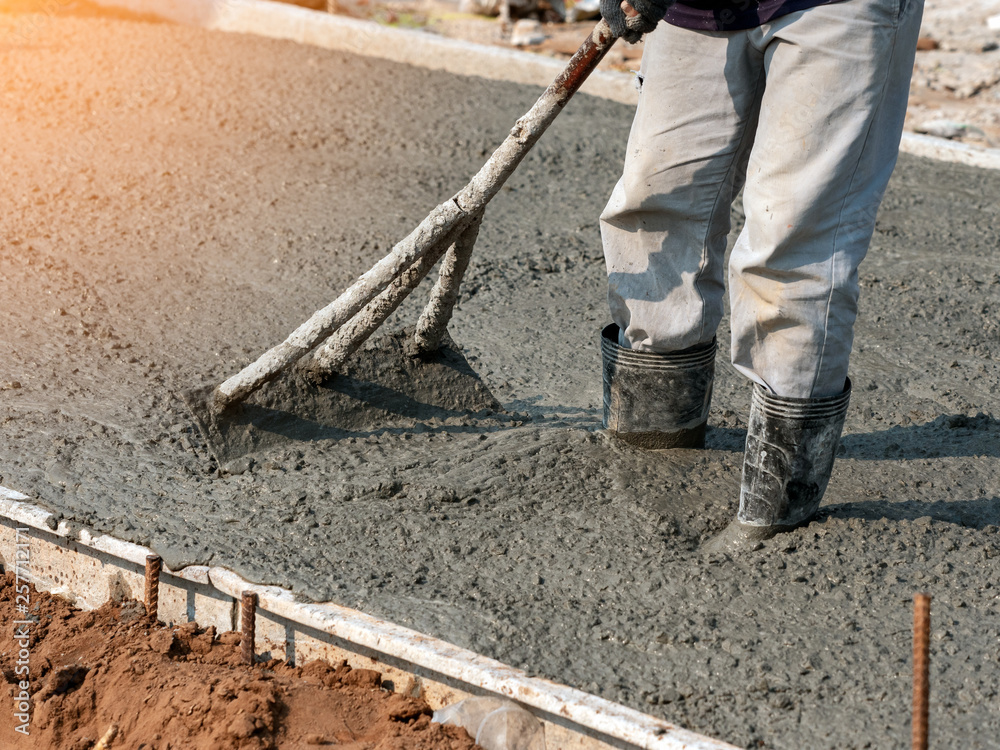 Workers adjust leveling of lean road concrete with hoe in construction site Workers adjust leveling of lean road concrete with hoe in construction site
