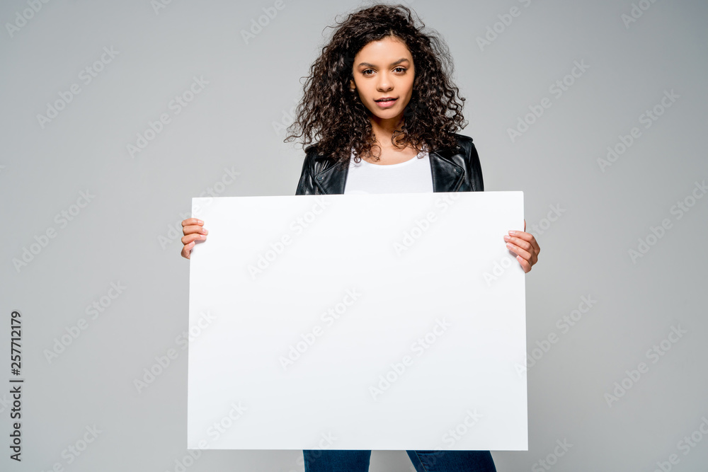 beautiful curly african american girl holding blank placard while standing isolated on grey