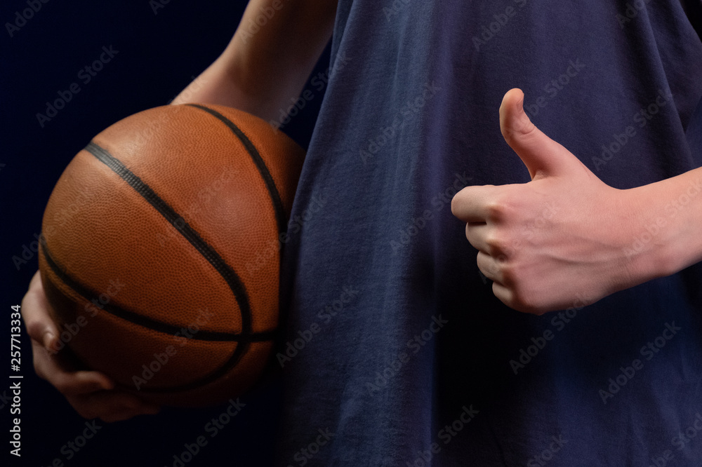 Basketball ball in teenager's hand and thumb up. Concept Success in sport. Great team game. Victory and a good winning score. Basketball advertising. Basketball ball in teenager's hand and thumb up. Concept Success in sport. Great team game. Victory and a good winning score. Basketball advertising.