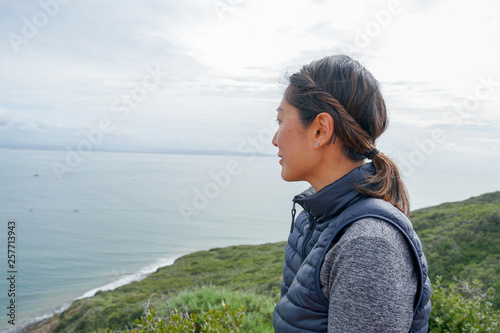 Young sporty Asian woman looking out at the beautiful ocean view. Young woman hiker standing admiring the view. healthy active lifestyle concept photo