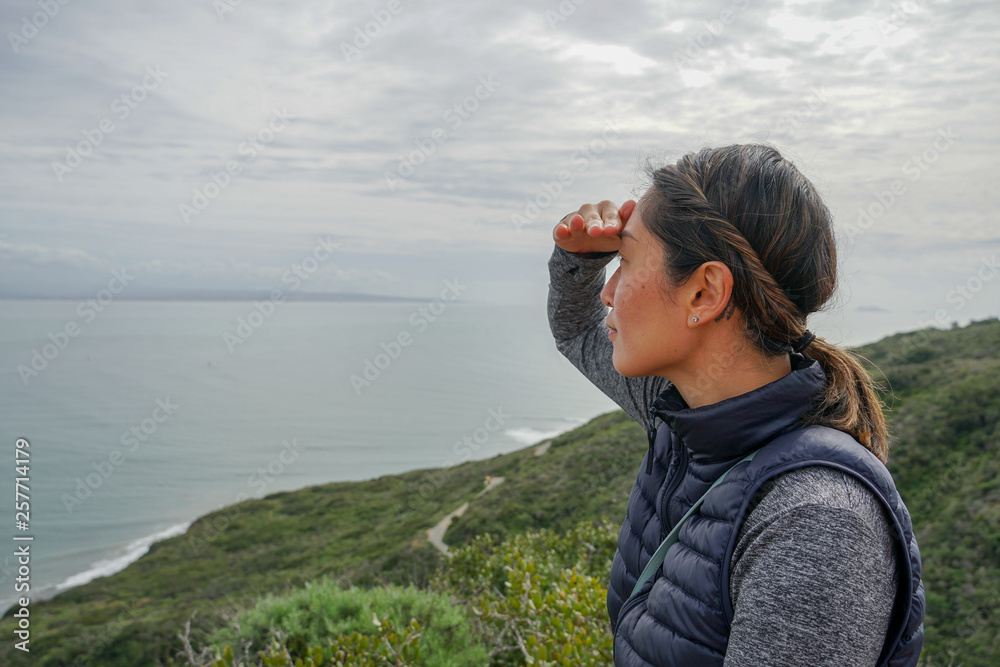 Young sporty Asian woman looking out at the beautiful ocean view. Young woman hiker standing admiring the view. healthy active lifestyle concept