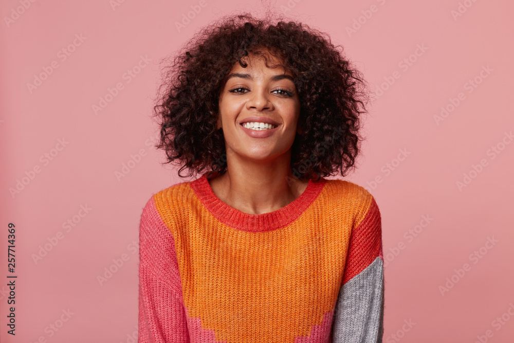 Positive optimistic charming african american girl looking swell wonderful playful confident joyful, with afro hairstyle, with lively smile, wearing colorful longsleeve, isolated on pink background Positive optimistic charming african american girl looking swell wonderful playful confident joyful, with afro hairstyle, with lively smile, wearing colorful longsleeve, isolated on pink background