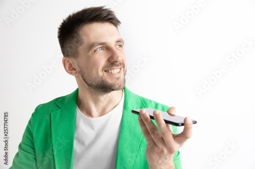 Indoor portrait of attractive young man isolated on gray background, holding smartphone, using voice control, feeling happy and surprised. Human emotions, facial expression concept.