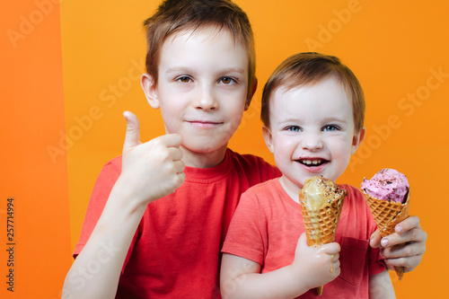 Laughing boys brothers eating ice cream cones  stay along on bright colorful background wall  have summer mood and laugh.