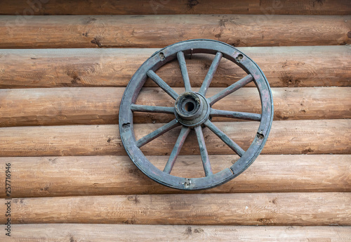 the old cartwheel hangs on the wall of a log house © ANDREI