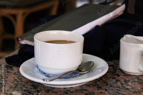 White small cup with coffee on a saucer on the table, with a notepad in the background