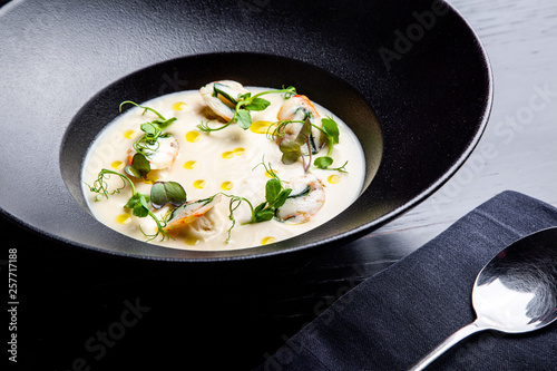 Cream soup is steaming in a black plate with on the black table. Photo for menu
