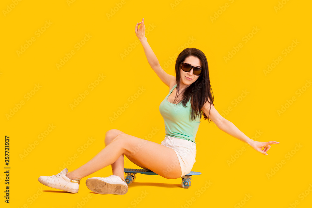 beautiful girl in sunglasses, sitting on a skateboard, image on yellow background, concept positive summer mood