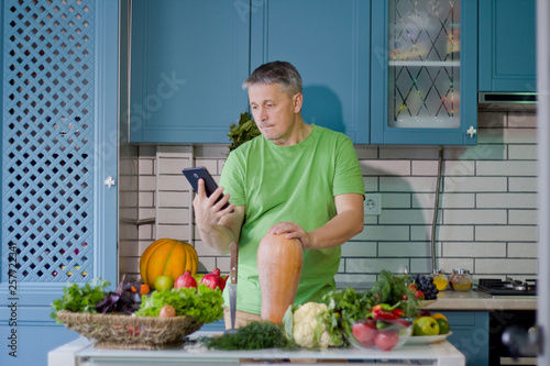 A man in the kitchen prepares vegetarian dishes. Looks up a recipe on the tablet display.