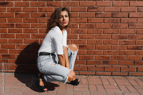 Fotografie Young magnificent girl with light-brown curly hair in white t-shirt and denim pa