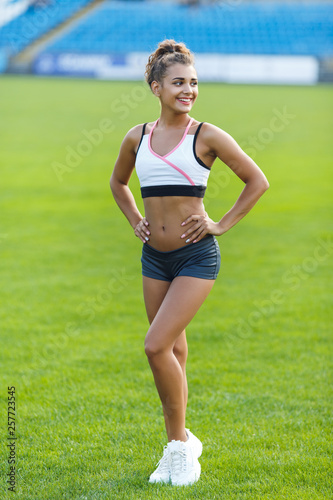 Young smiling beautiful girl in trendy sportswear with hands on waist