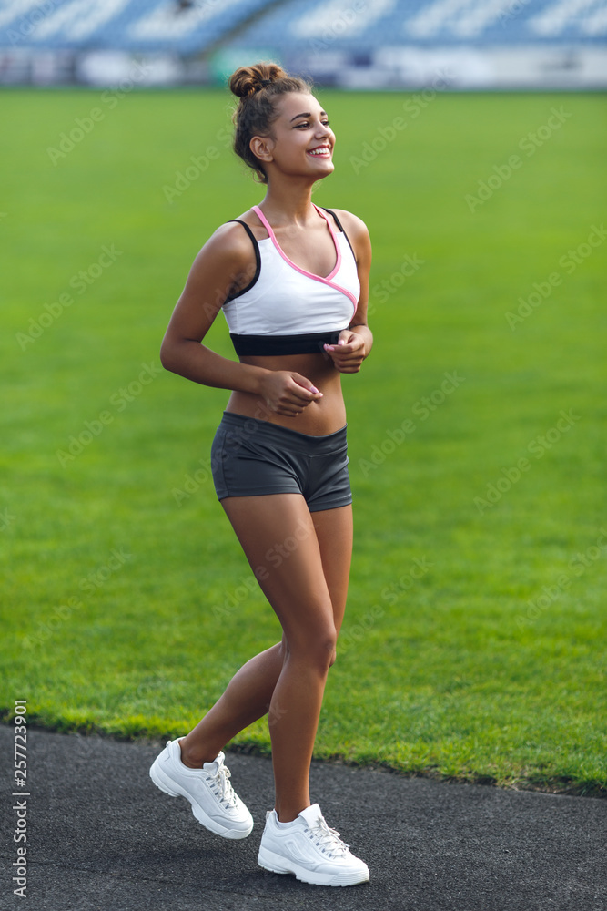 Young smiling girl with bronze tan wearing sportswear runs in the stadium Young smiling girl with bronze tan wearing sportswear runs in the stadium
