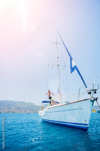 Boy jump in sea of sailing yacht on summer cruise. Travel adventure  yachting with child on vacation.