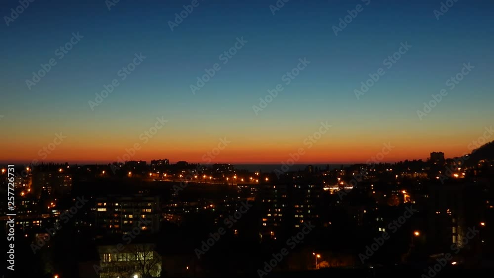 Sunset time lapse over the sea and evening city. Thickening of colors. The lights of the city are lit at dusk Sunset time lapse over the sea and evening city. Thickening of colors. The lights of the city are lit at dusk