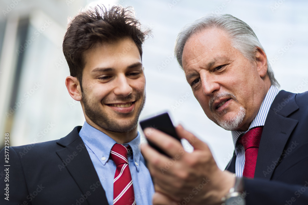 Senior manager showing something on a smartphone to his younger colleague Senior manager showing something on a smartphone to his younger colleague