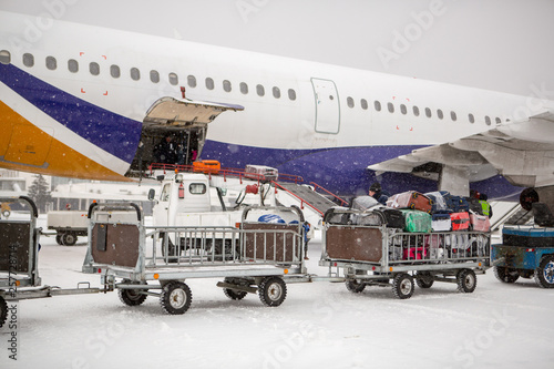 baggage loading at airport in winter. Luggage in carts near aircraft in winter. Passenger aircraft in winter at airport loaded baggage before departure.