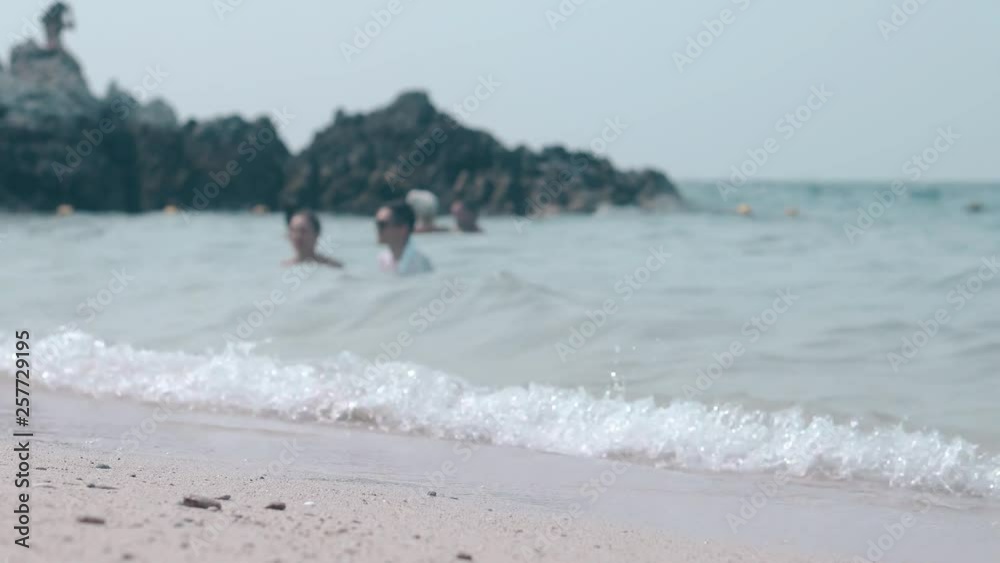 yellow sandy beach washed by ocean foaming waves against swimming people and brown rock in tropics yellow sandy beach washed by ocean foaming waves against swimming people and brown rock in tropics