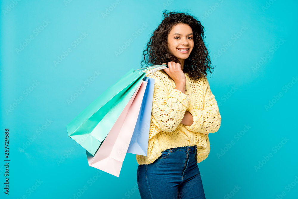 cheerful curly african american girl holding shopping bags while standing isolated on blue cheerful curly african american girl holding shopping bags while standing isolated on blue