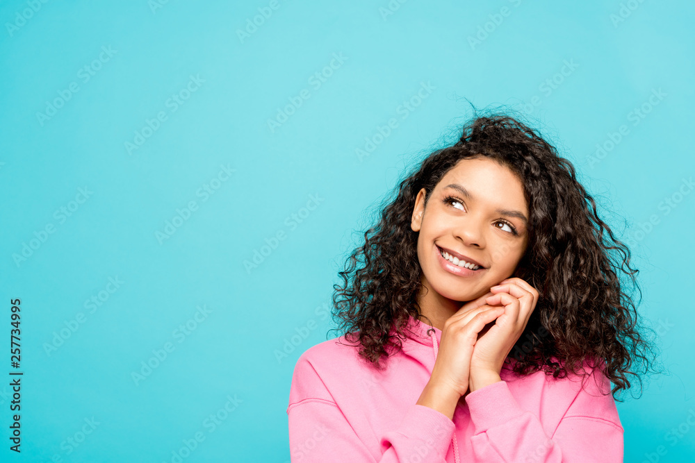 dreamy curly african american girl smiling while standing isolated on blue dreamy curly african american girl smiling while standing isolated on blue