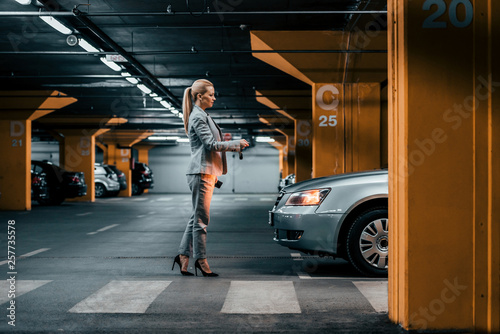 Elegant businesswoman with car keys in front of a car in underground parking. © bnenin