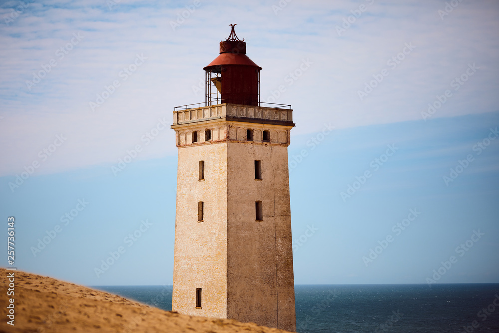 Scenery of Rubjerg Knude Fyr Lighthouse in Lønstrup Klint cliff, Denmark, located on North Sea coast, surrounded by sand dunes and viewed from the mainland