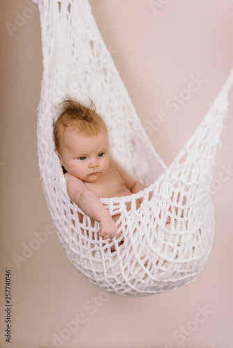 Newborn Baby relaxing in a white hammock with soft bright background - happy family moments