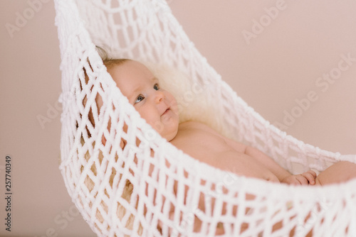 Newborn Baby relaxing in a white hammock with soft bright background - happy family moments
