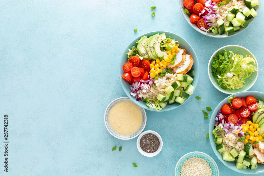 Lunch bowls with grilled cgicken meat, rice and fresh salad of avocado, cucumbers, corn, tomato and onion