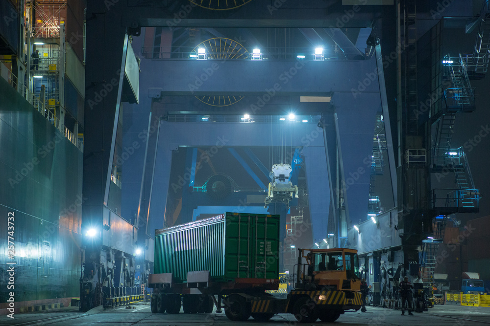 operation of container terminal at night. Unloading container ship at night. Mooring cranes unload container ship at night