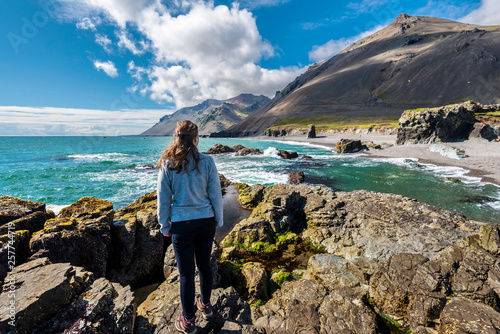 Girl teenager is staying on the stone facing to Fauskasandur beach in the eastern Iceland. Maelifell hill is at right background.